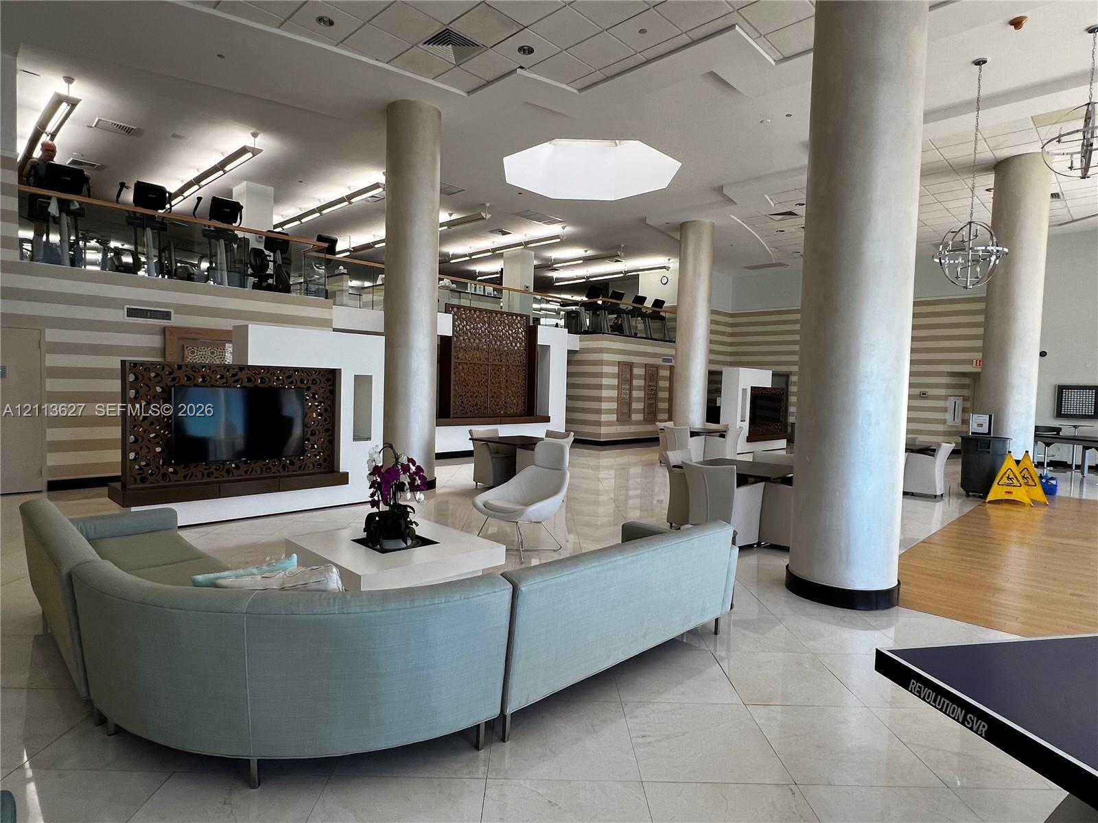 Spacious common area featuring large structural columns, polished stone flooring, intricate laser-cut wood privacy screens, and overhead geometric lighting fixtures