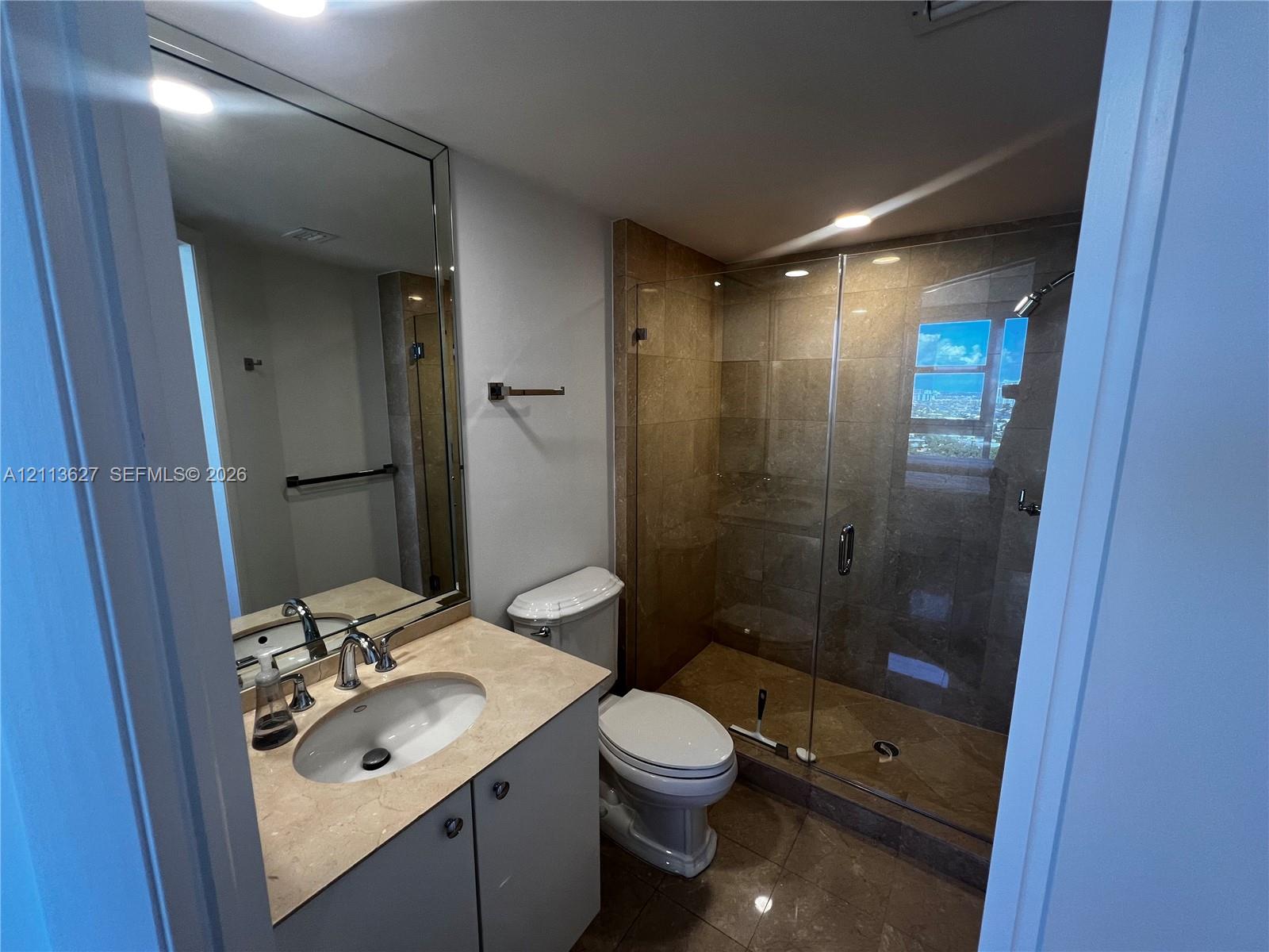 Bathroom featuring a stone-surface vanity with an integrated basin, large wall-mounted mirror, and a walk-in shower with stone tile surround and glass enclosure