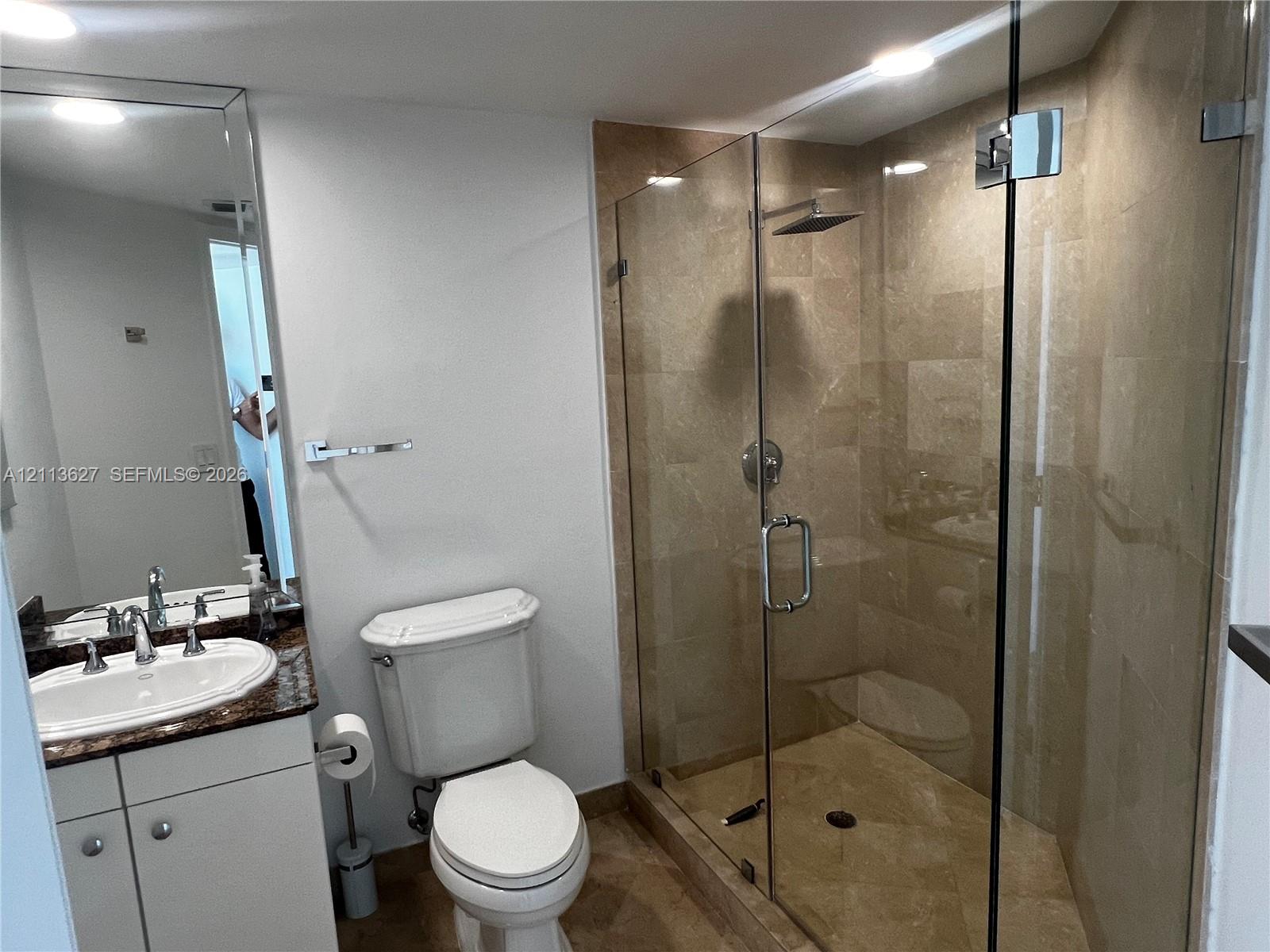 Bathroom featuring a walk-in shower with glass enclosure, tiled surround, and overhead rainfall fixture, complemented by a vanity with a stone countertop and an inset sink