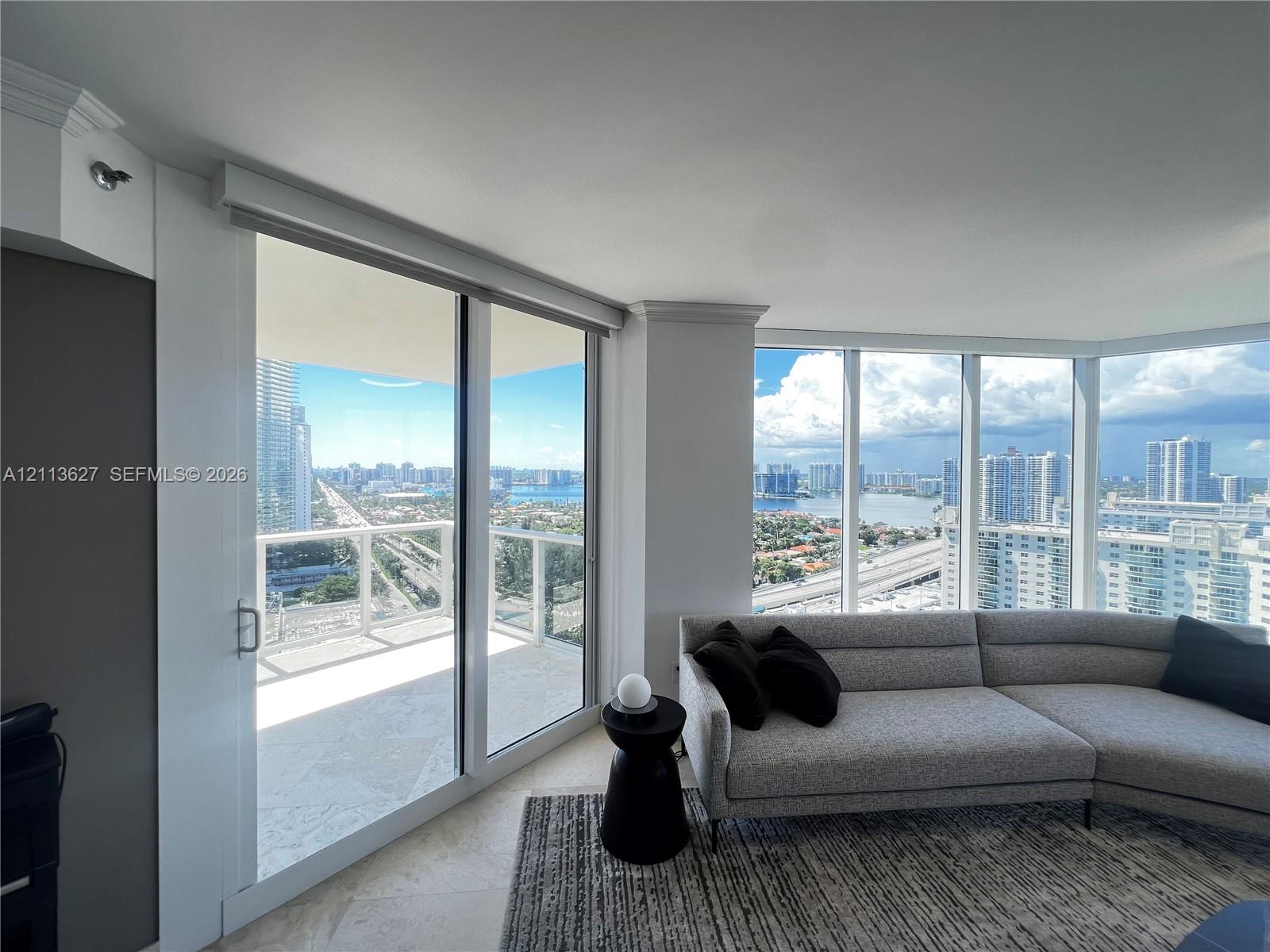 Floor-to-ceiling windows, sliding glass door, private balcony, and light-tone stone flooring