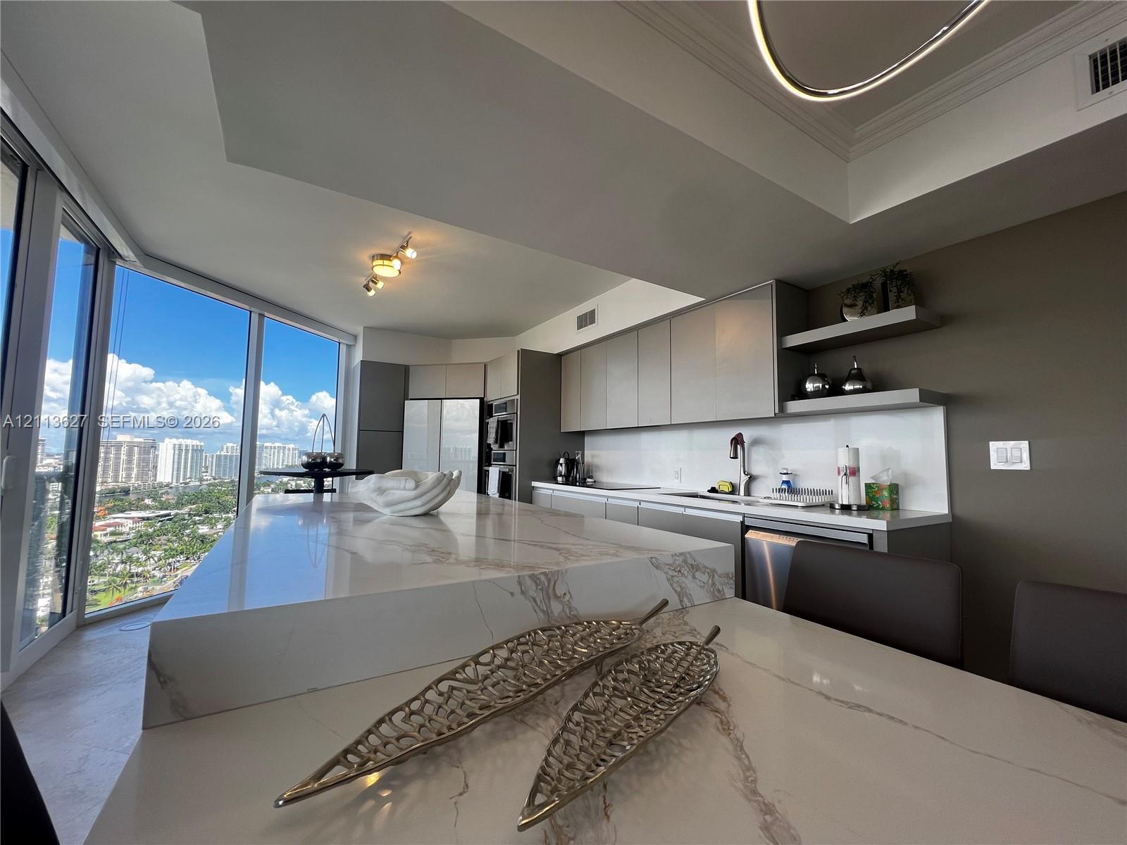 Kitchen featuring a waterfall-edge island with stone-finish countertop, flat-panel cabinetry, open shelving, integrated stainless steel appliances, and floor-to-ceiling glass windows