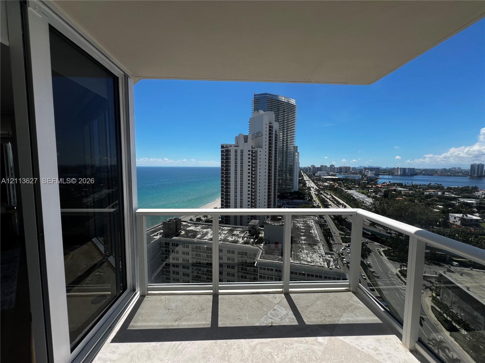 Private balcony featuring stone flooring, a white metal railing with glass panels, and sliding glass doors
