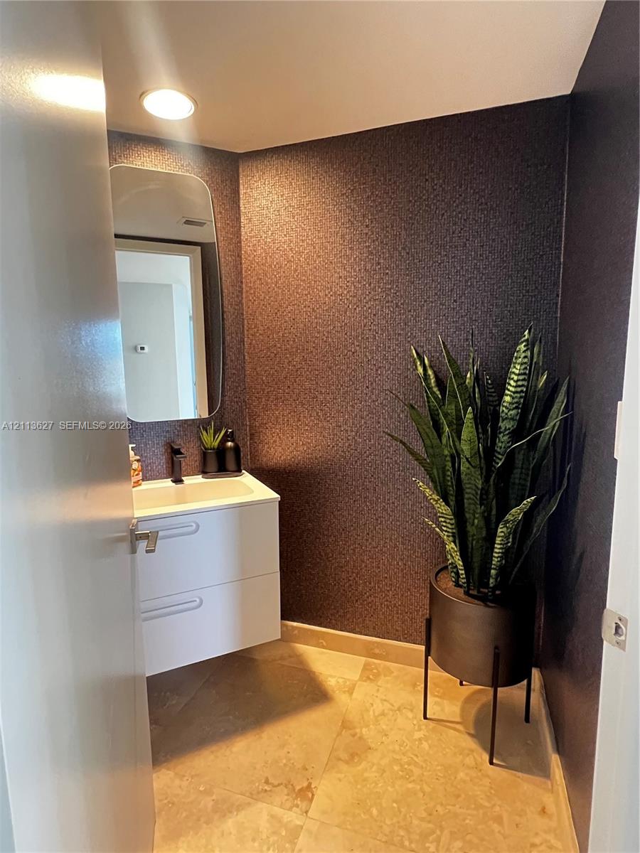 Modern white floating vanity featuring dual handleless drawers, integrated rectangular sink basin, and dark faucet hardware, complemented by textured dark accent walls and tile flooring