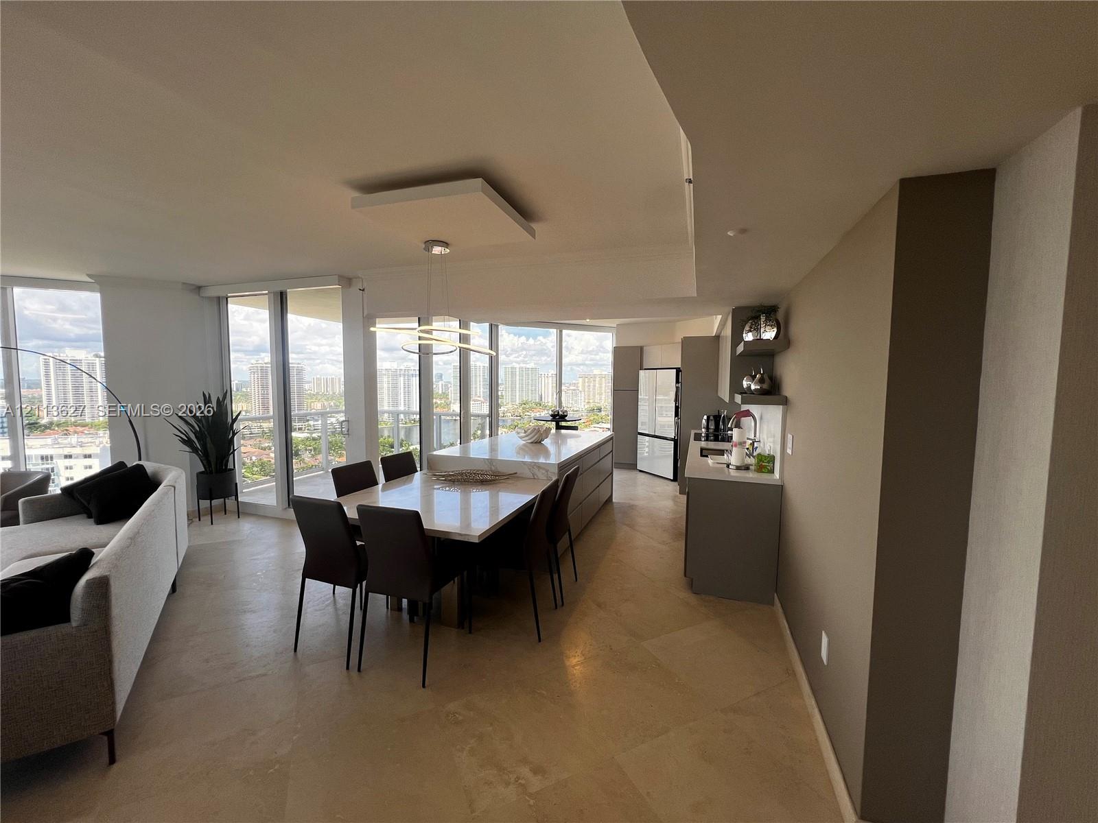 Open-concept kitchen and dining area featuring large-format stone flooring, floor-to-ceiling windows, center island with stone countertop, and built-in cabinetry
