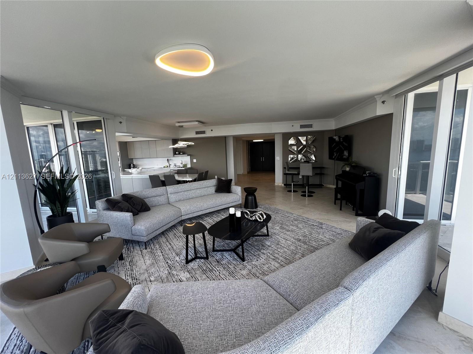 Open-concept living area featuring stone-finish flooring, floor-to-ceiling glass panel doors, custom recessed ceiling lighting, and minimalist built-in cabinetry