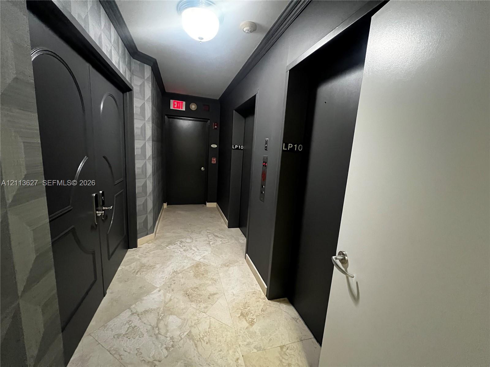 Stone tile flooring, geometric textured wall covering, double-door entry with metallic hardware, dual elevator access, and monochromatic architectural detailing