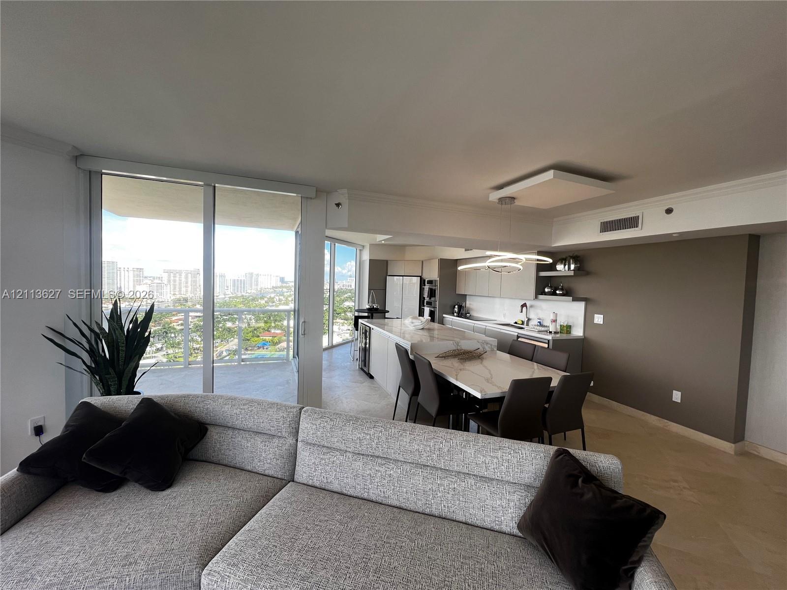 Open-concept kitchen featuring an oversized island with stone-finish countertops, flat-panel cabinetry, built-in stainless steel appliances, and floor-to-ceiling glass sliding doors
