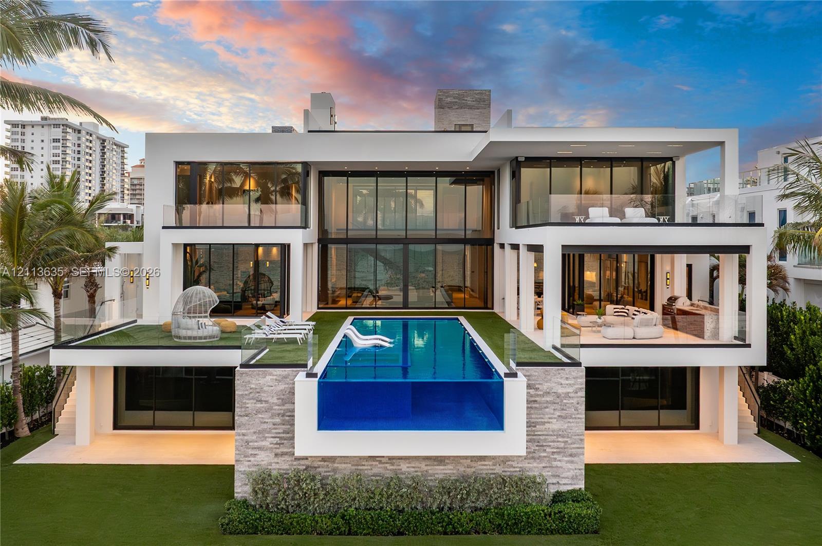 Contemporary multi-level residence featuring floor-to-ceiling glass walls, an elevated infinity-edge pool with a transparent side panel, stacked stone exterior accents, and expansive private balconies with glass railings