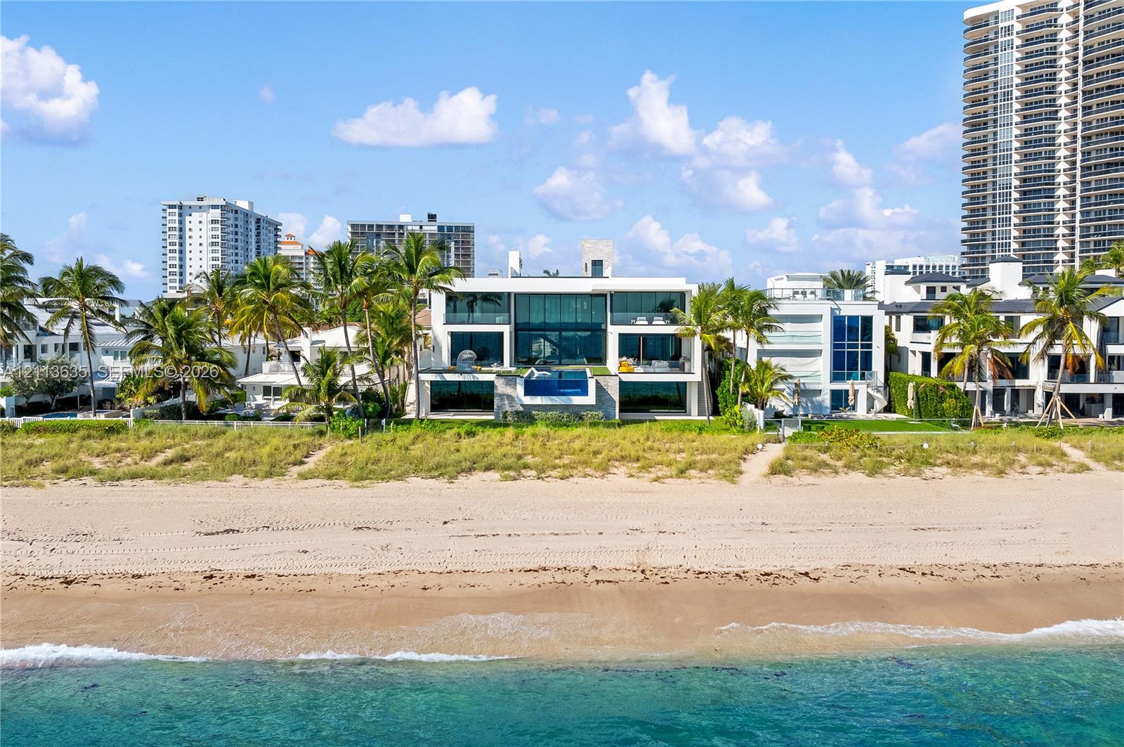 Contemporary oceanfront estate featuring floor-to-ceiling glass walls, elevated infinity-edge swimming pool, expansive structural overhangs, and direct beach access