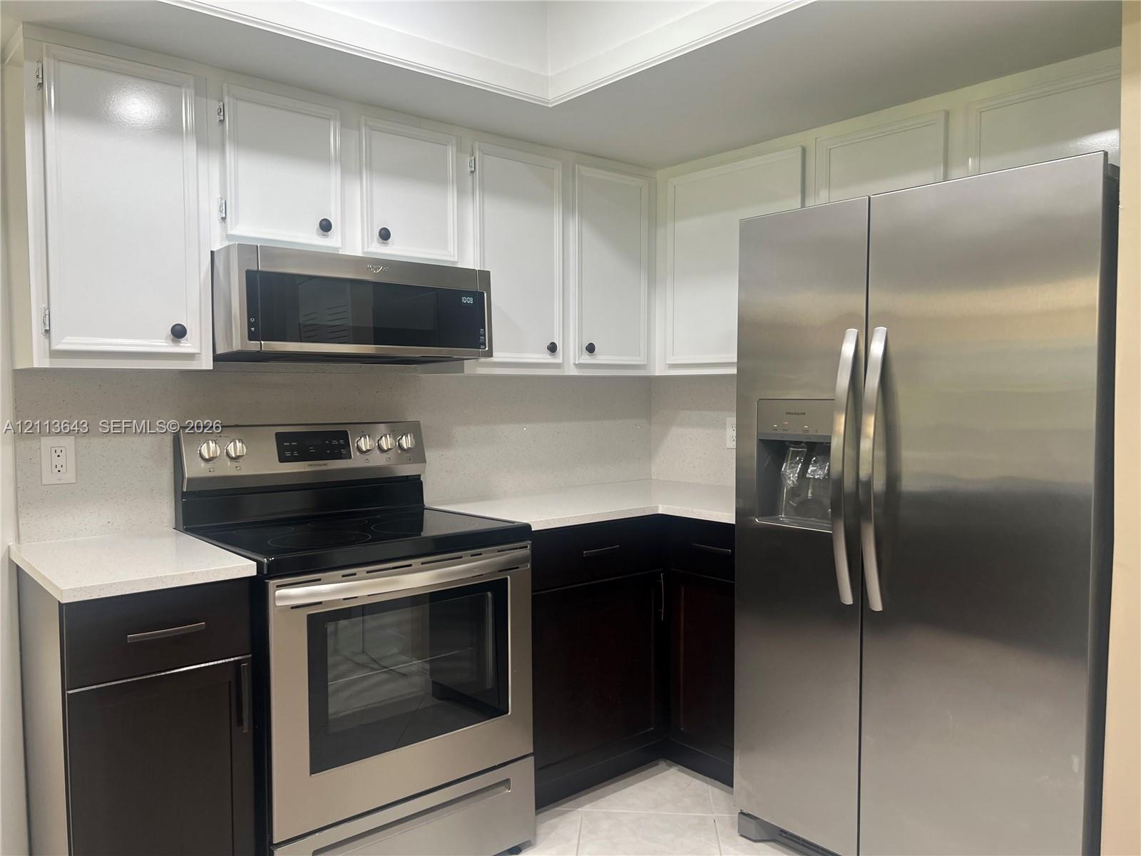 Kitchen featuring white upper cabinetry, dark lower cabinetry, light-toned stone-finish countertops, and stainless steel appliances including a range, microwave, and refrigerator