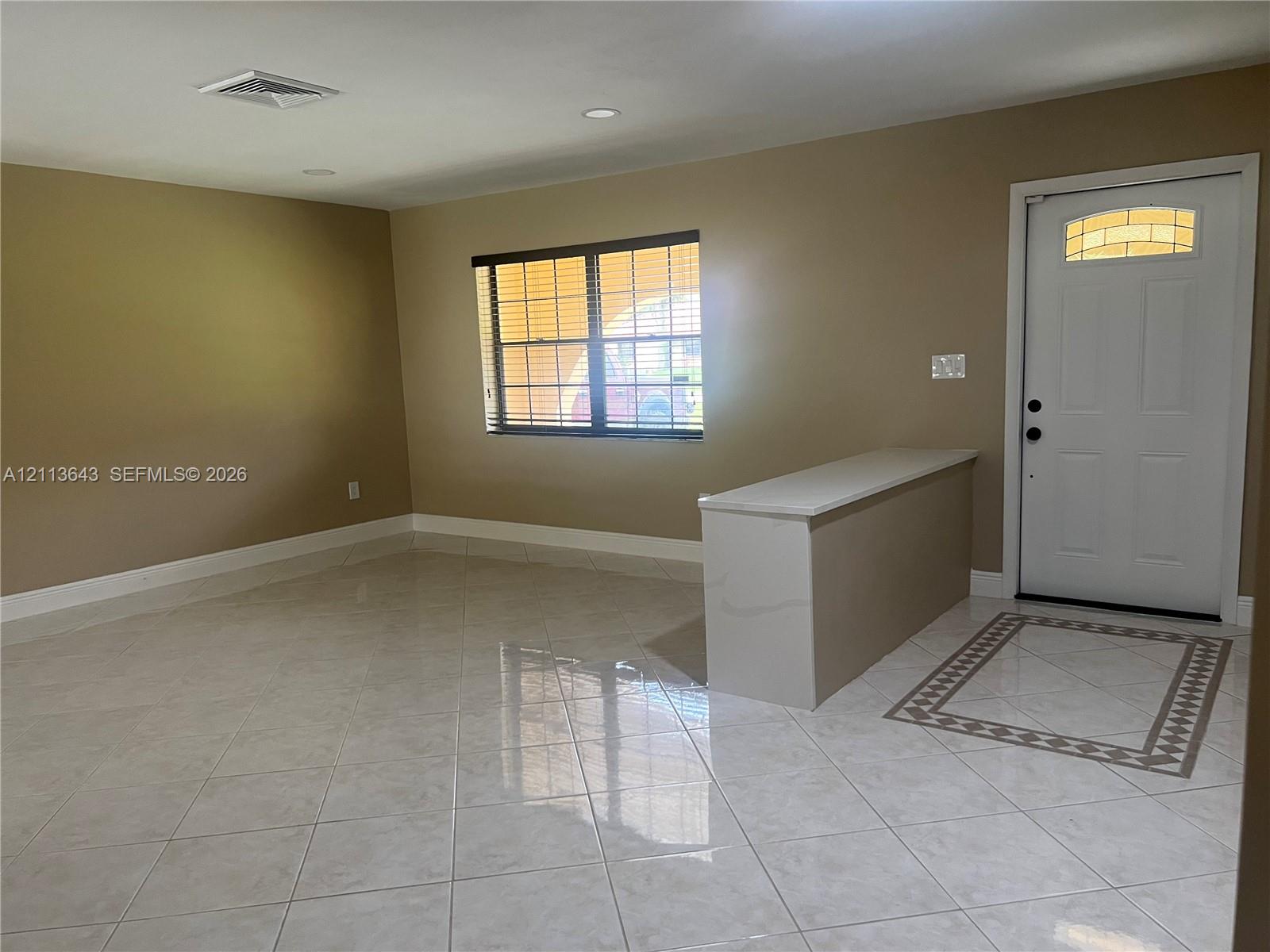 Neutral-toned interior featuring large-format ceramic tile flooring, a built-in counter with a stone-finish top, an exterior door with a decorative transom window, and a multi-pane window