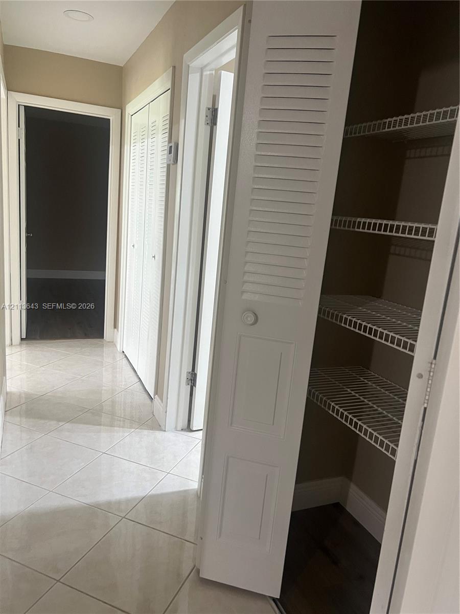 Hallway featuring diagonal-set ceramic tile flooring, louvered closet doors, and interior storage with built-in wire shelving