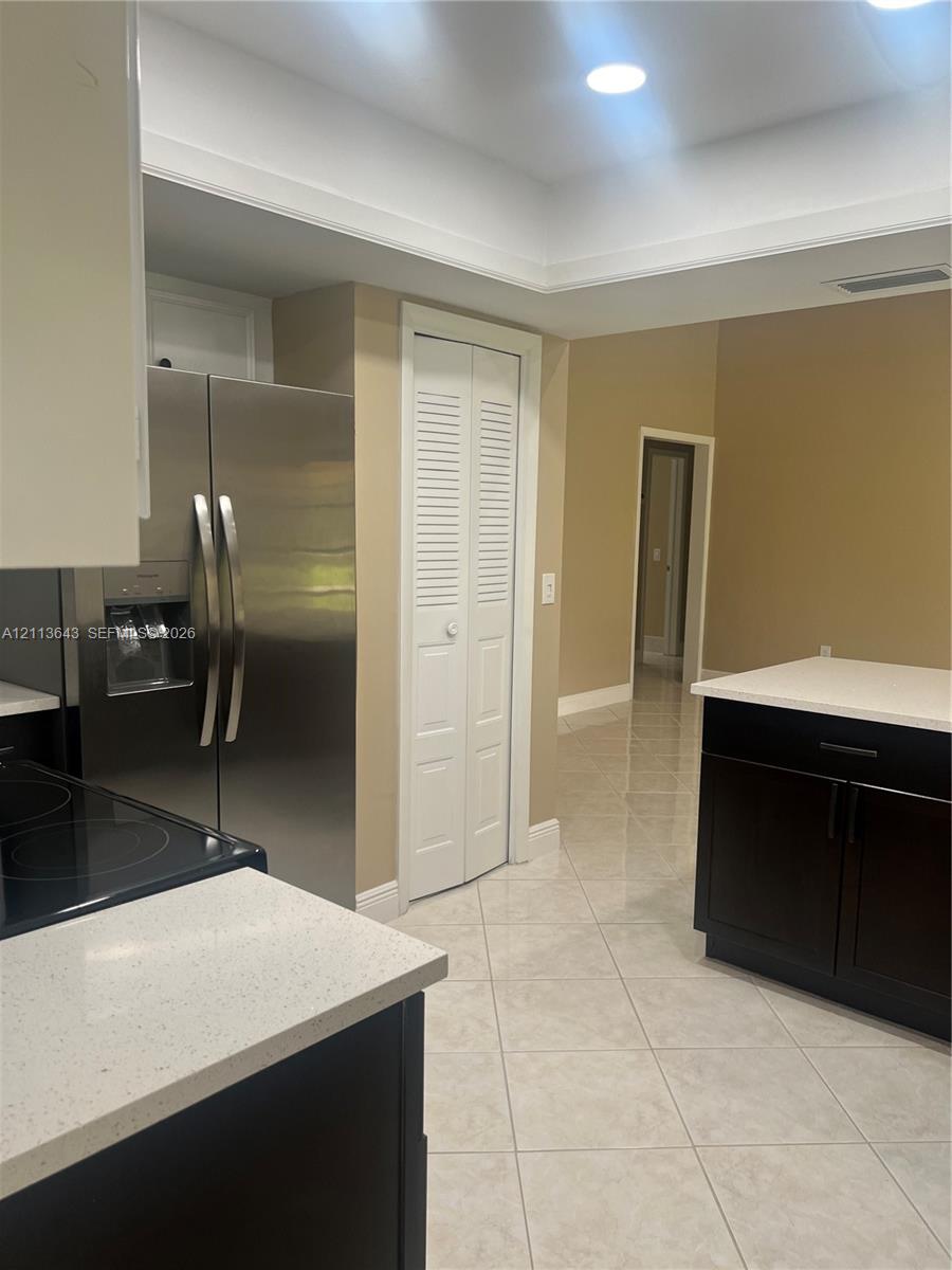 Kitchen featuring dark cabinetry, light-toned solid surface countertops, stainless steel side-by-side refrigerator, recessed lighting, and tile flooring