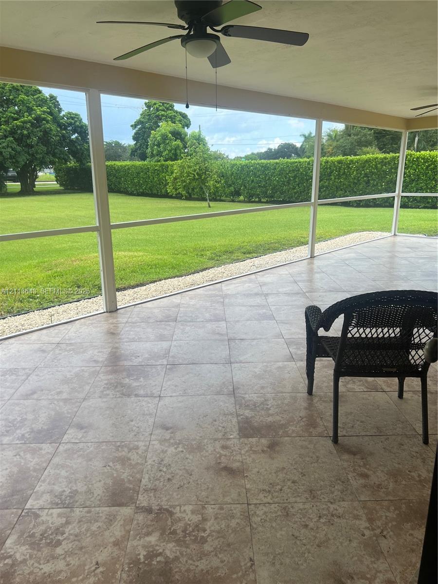 Screened lanai featuring large-format stone-look tile flooring, ceiling fans, and a expansive backyard with a manicured lawn and perimeter hedges