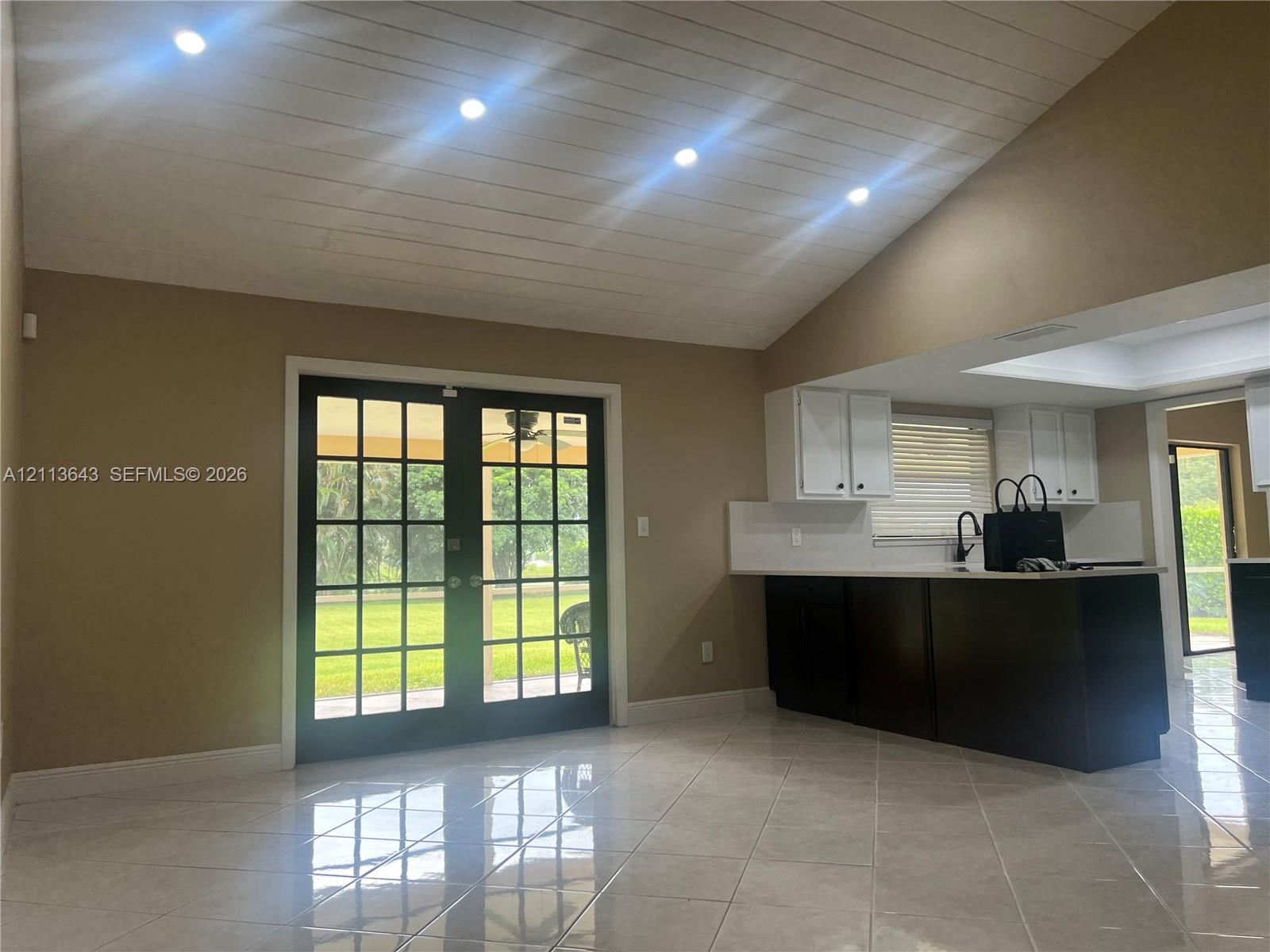 Vaulted ceiling with shiplap detailing, recessed lighting, tile flooring, glass-paneled double doors, and two-tone cabinetry with solid-surface countertops
