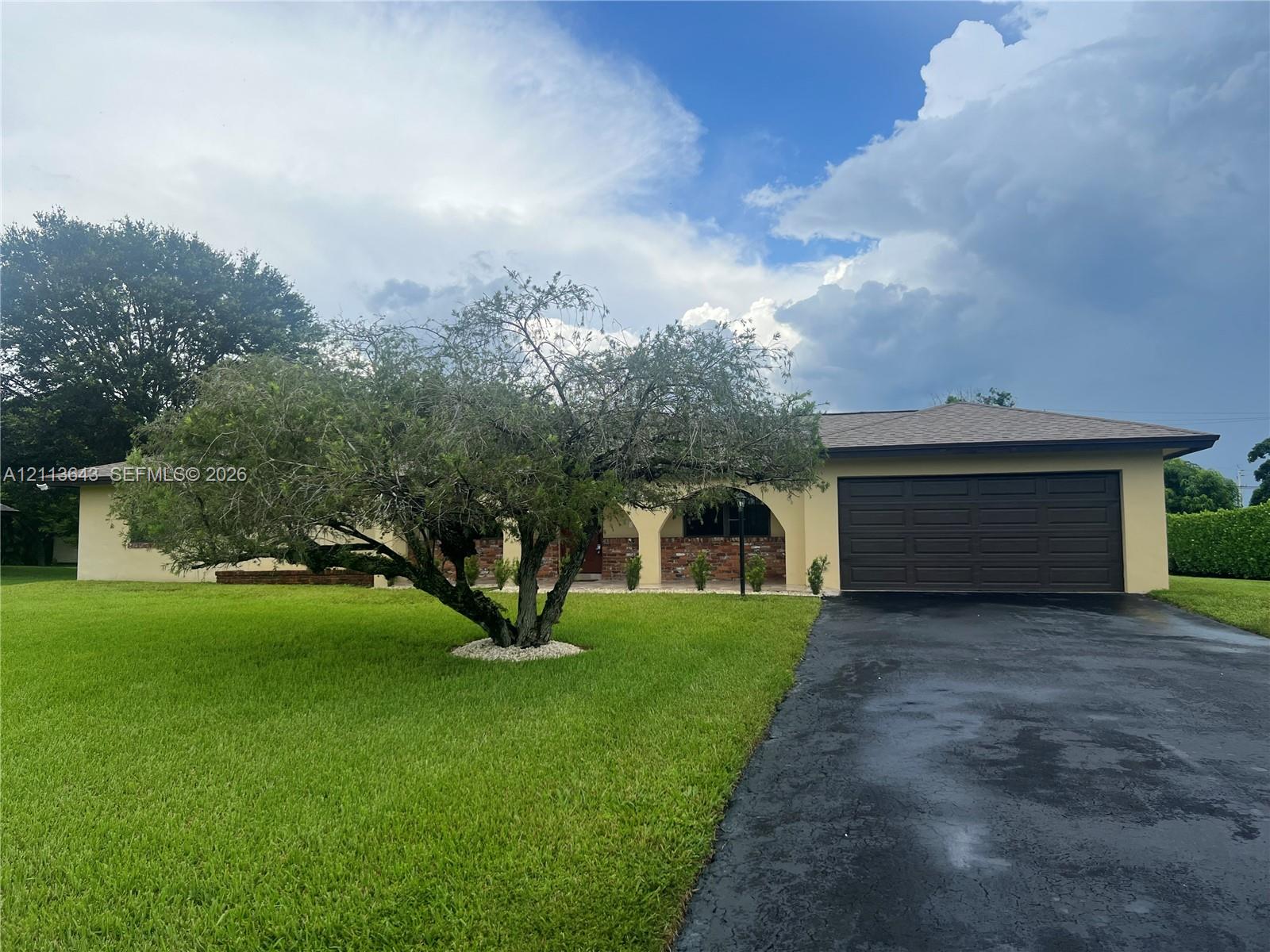 Single-story exterior featuring a brick facade, arched entryway, asphalt driveway, and a two-car garage