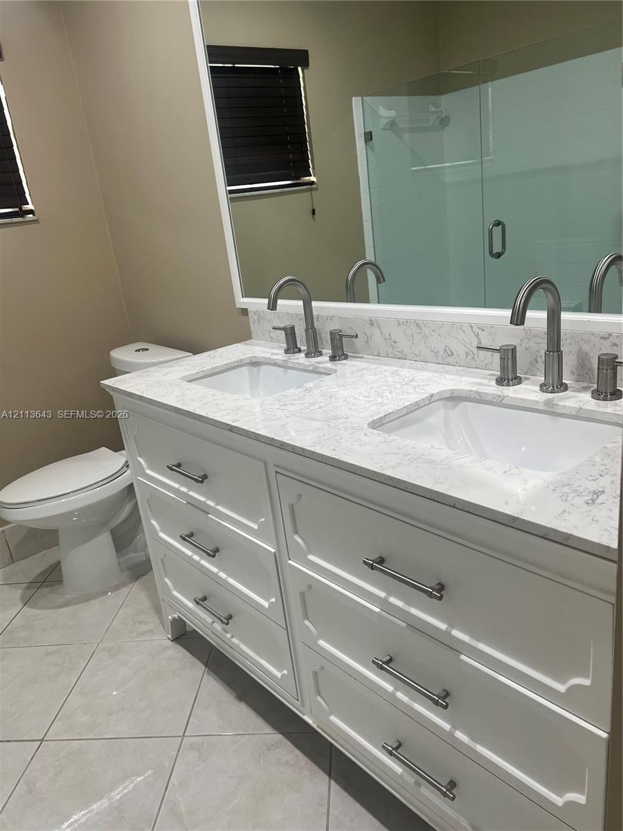 Dual-sink vanity with white cabinetry, light-toned stone-finish countertop, undermount rectangular sinks, brushed nickel hardware, and large wall-to-wall mirror