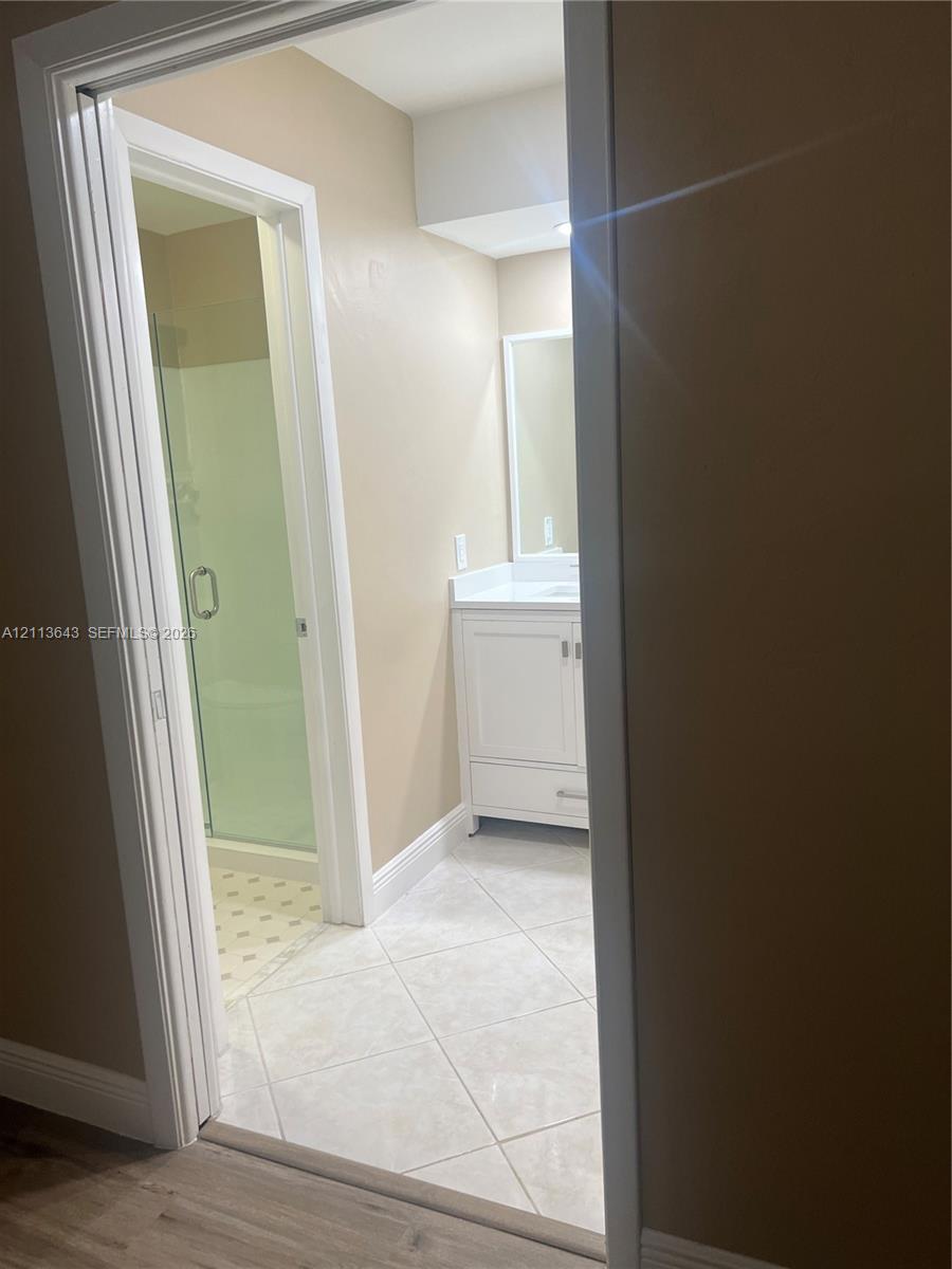 Bathroom featuring a white vanity cabinet with a stone-top integrated sink, a framed wall mirror, and a walk-in shower with a glass door and neutral tile flooring