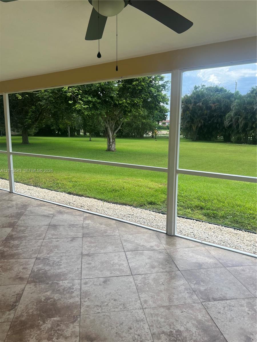 Screened-in patio featuring tile flooring, a ceiling fan, and access to a landscaped backyard with mature trees