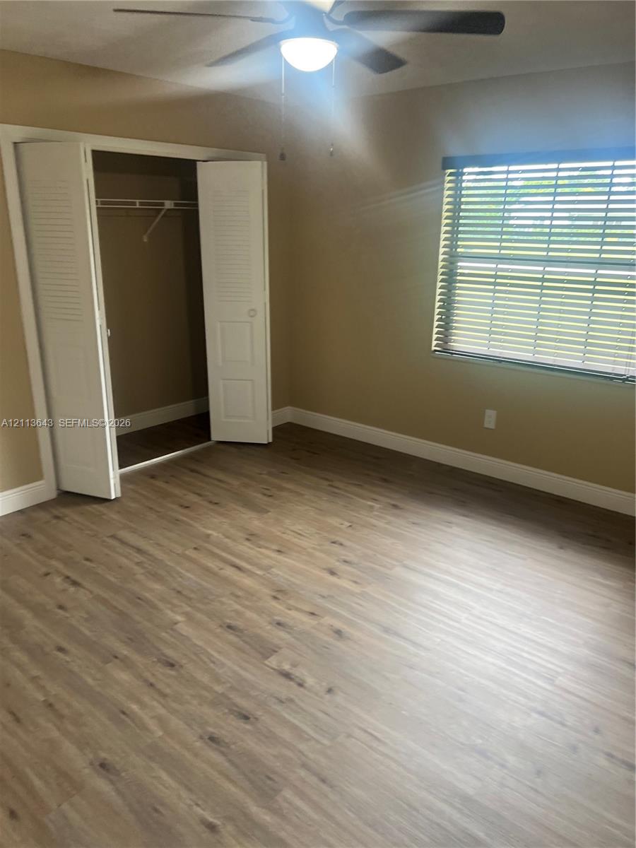 Interior space featuring wood-finish flooring, a ceiling fan with light fixture, a window with horizontal blinds, and a closet with bifold louvered doors