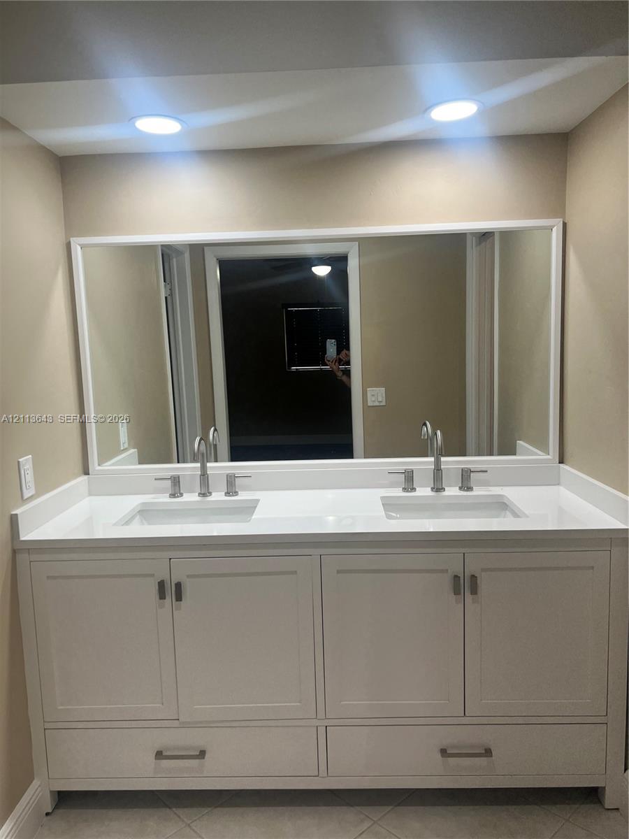 Double vanity featuring white cabinetry, a solid-surface countertop, dual rectangular undermount sinks, polished metal widespread faucets, and a full-width framed mirror