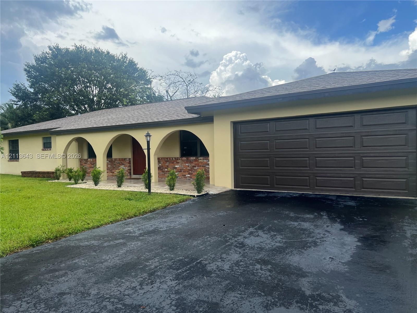 Single-story exterior featuring arched porticos, brick masonry accents, a paved driveway, and an attached multi-car garage