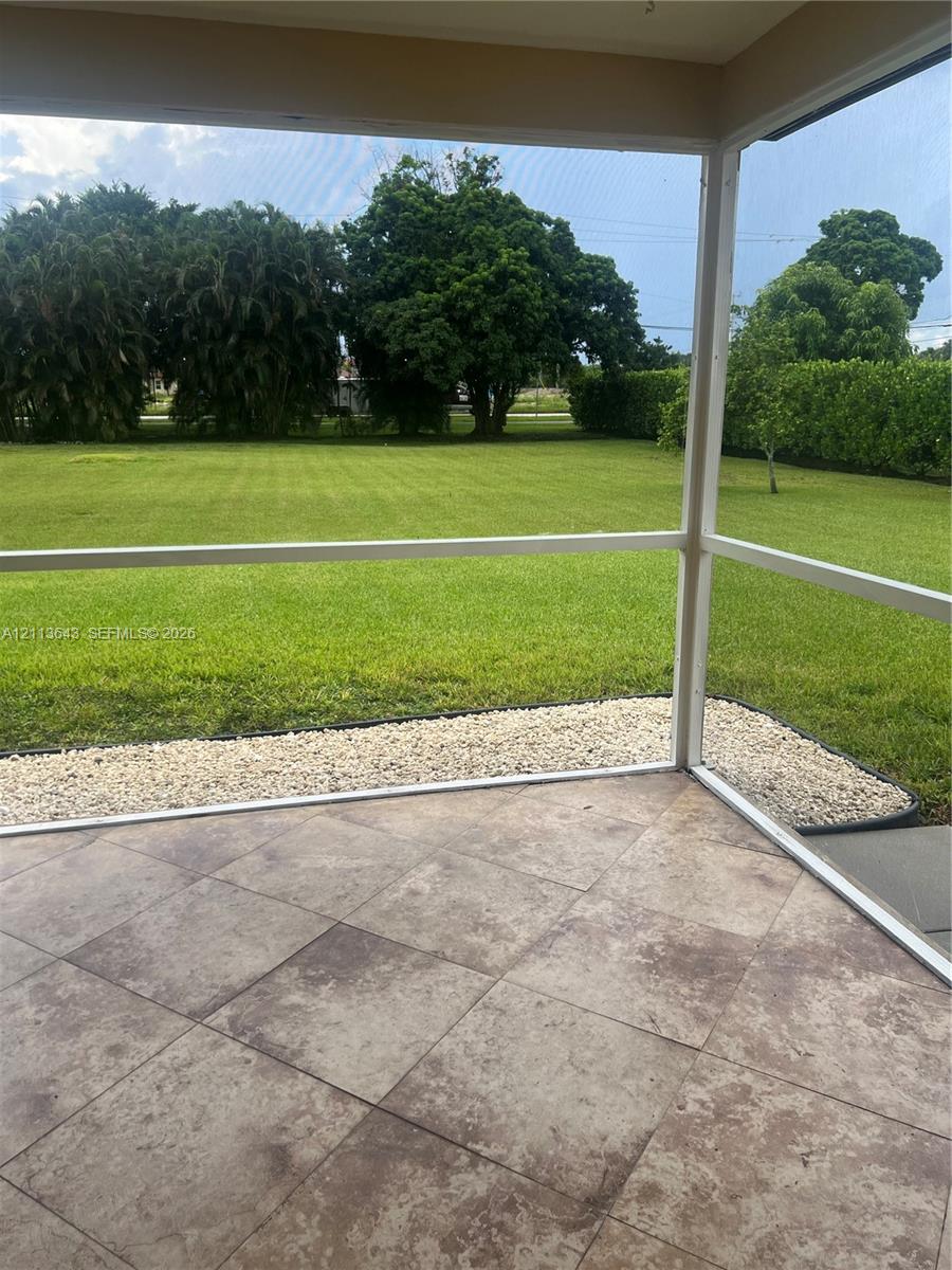 Screened-in patio with large-format tile flooring, perimeter stone landscaping, and an expansive lawn