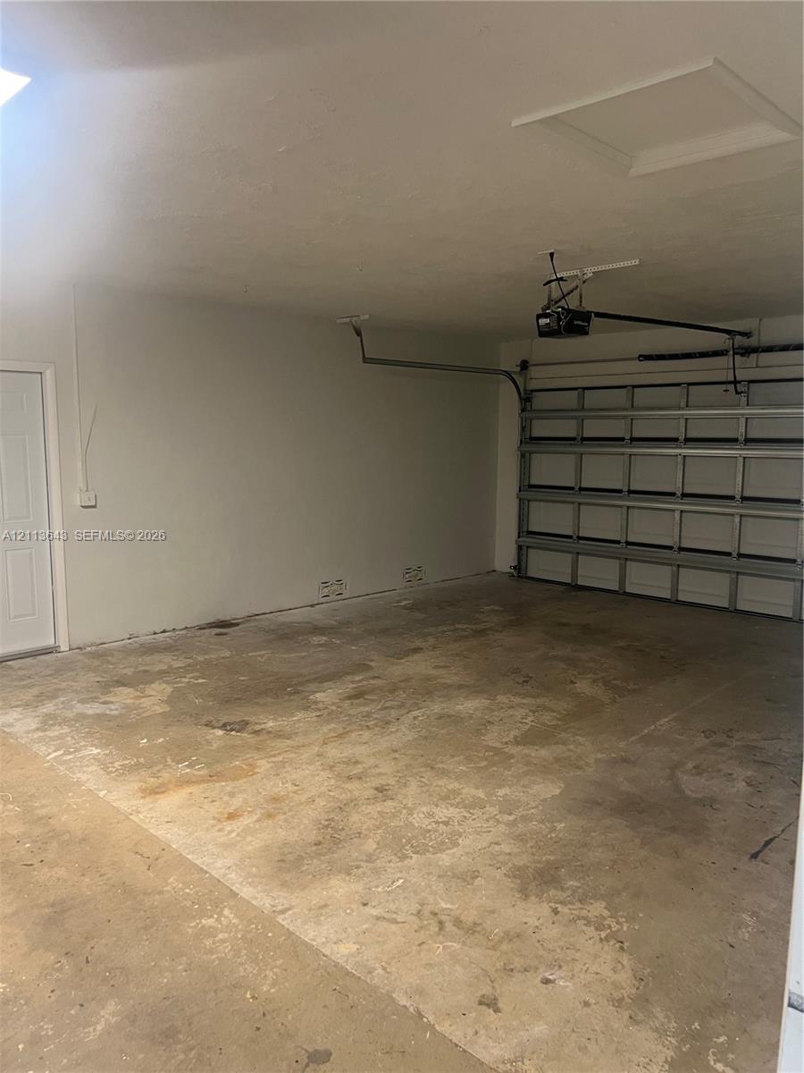 Garage featuring a concrete floor, sectional overhead door, automated garage door opener, and a separate pedestrian access door