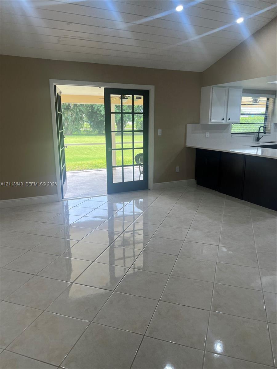 Tiled flooring, vaulted ceiling with wood-plank finish, recessed lighting, glass-paned French doors, and cabinetry with contrasting countertops
