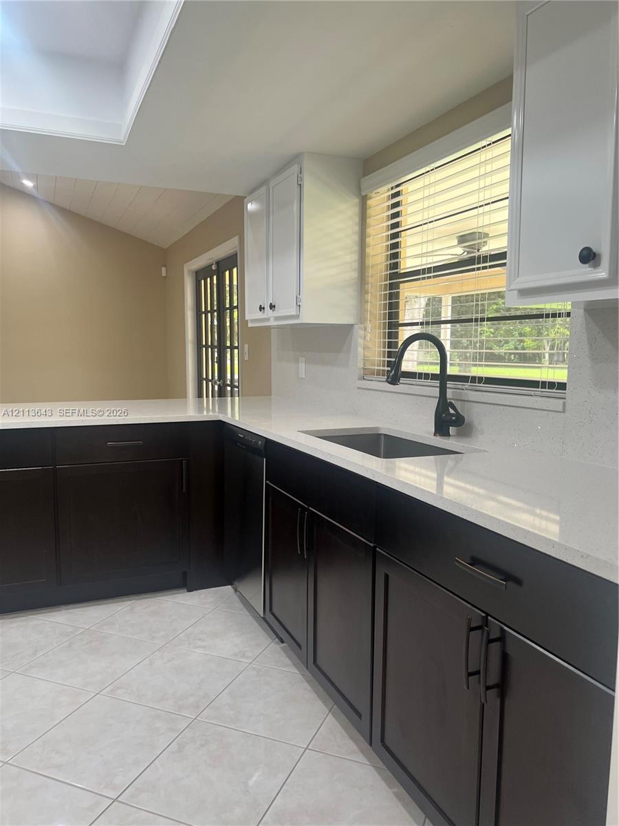 Kitchen featuring high-contrast cabinetry, stone countertops, stainless steel sink with matte black gooseneck faucet, tile flooring, and a glass-paned exterior door