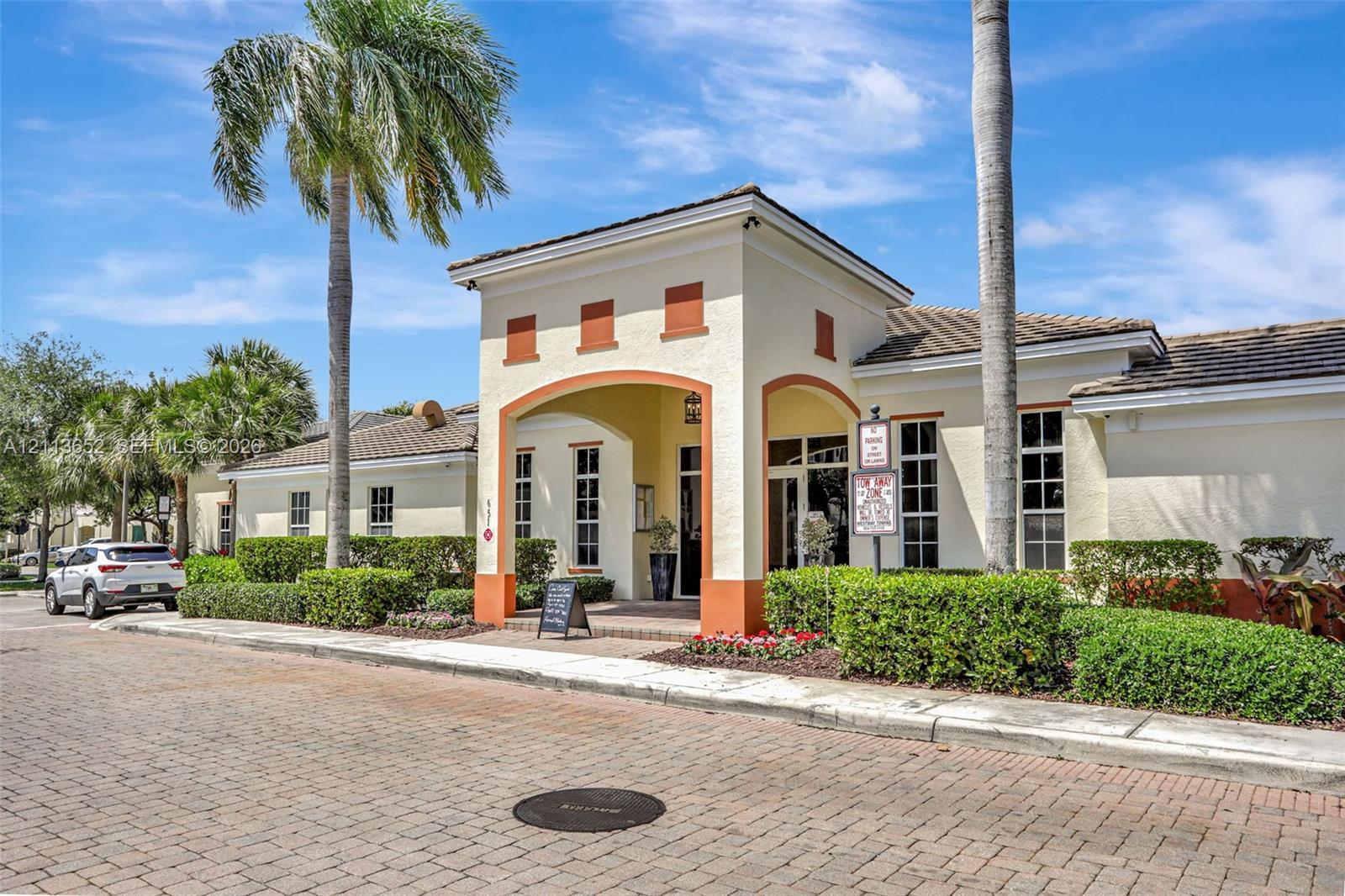 Stucco exterior featuring an arched entryway, decorative trim, tile roof, and brick-paver street