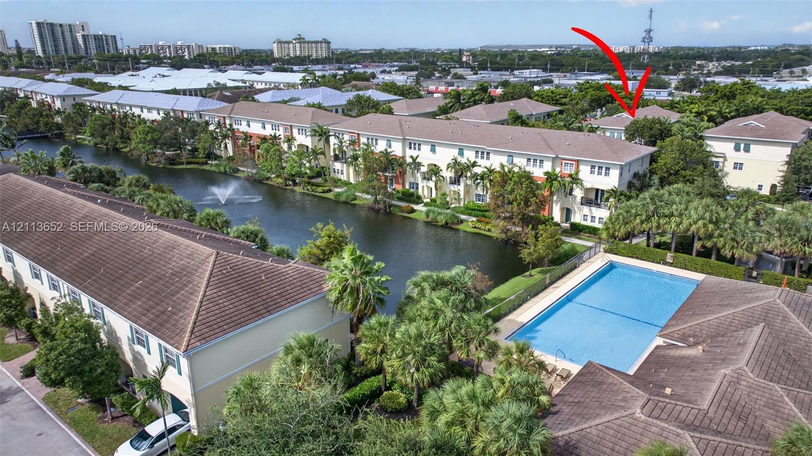 Aerial perspective featuring waterfront placement, community pool, mature palm landscaping, and tile roofing