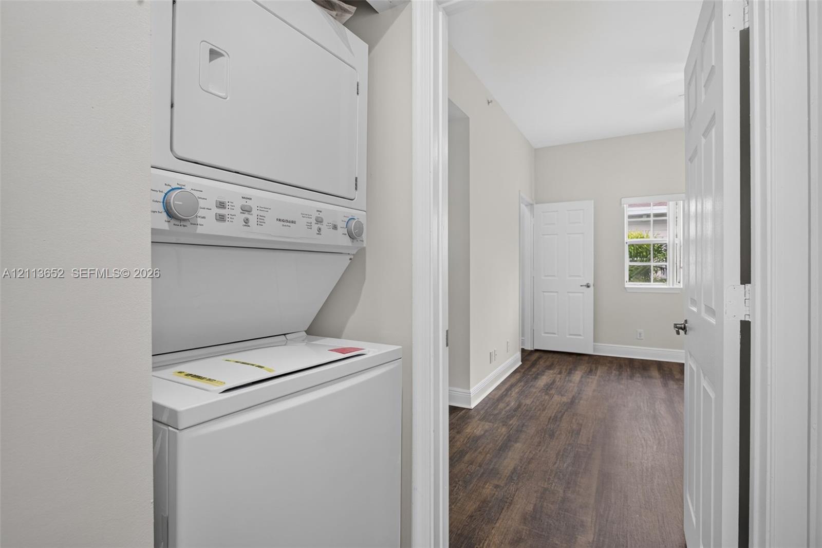 Stacked laundry appliance, wood-finish flooring, white panel doors, and a single-pane window