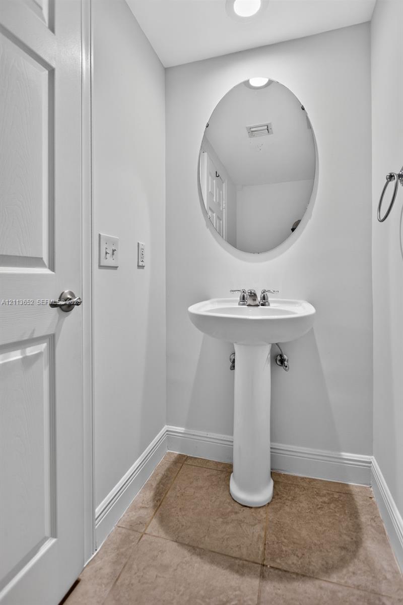 White porcelain pedestal sink, oval wall-mounted mirror, metal faucet hardware, and neutral tile flooring