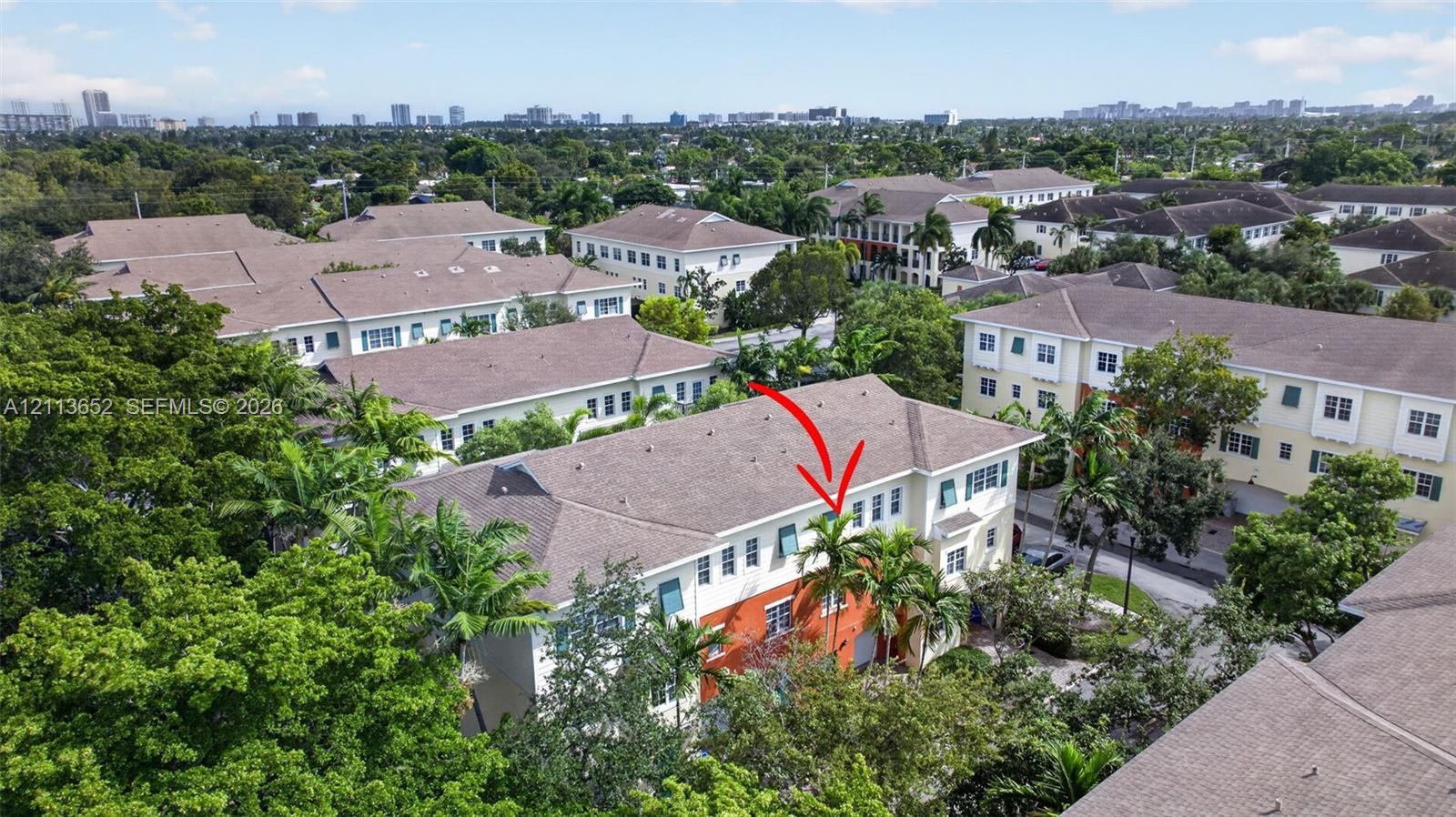 Multi-level townhouse featuring a shingled roof, stucco exterior with vibrant accents, decorative window shutters, and established perimeter landscaping