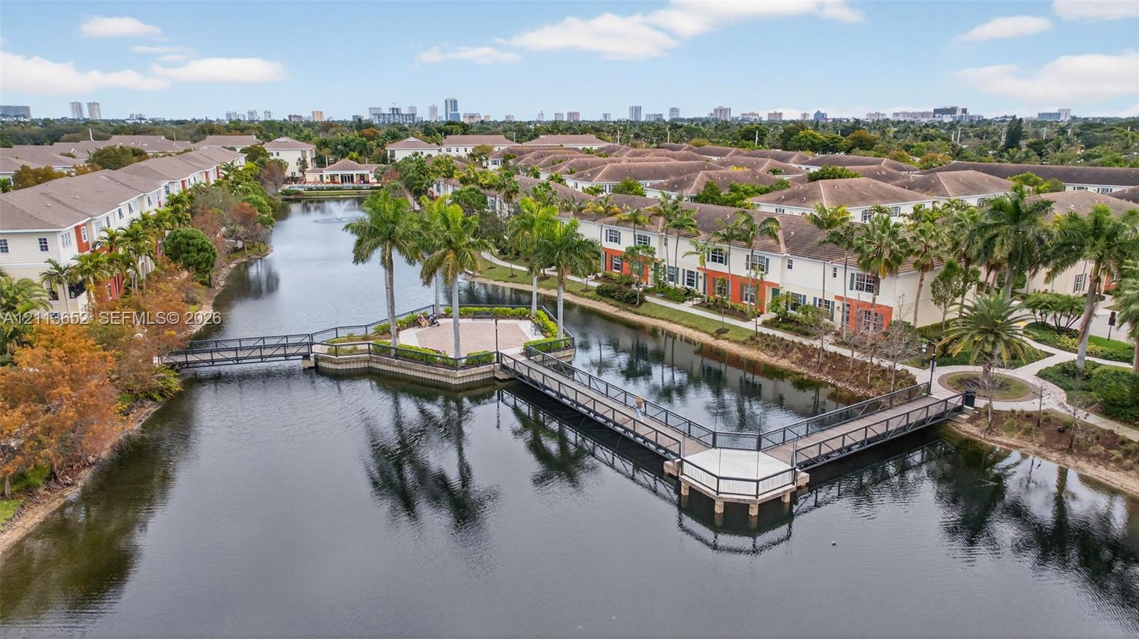 Community lake featuring pedestrian footbridges, a paved central gazebo, and manicured palm tree landscaping