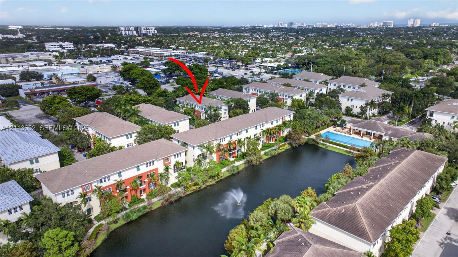 Aerial perspective of residential community featuring a water feature with fountain, mature landscaping, and common-area swimming pool