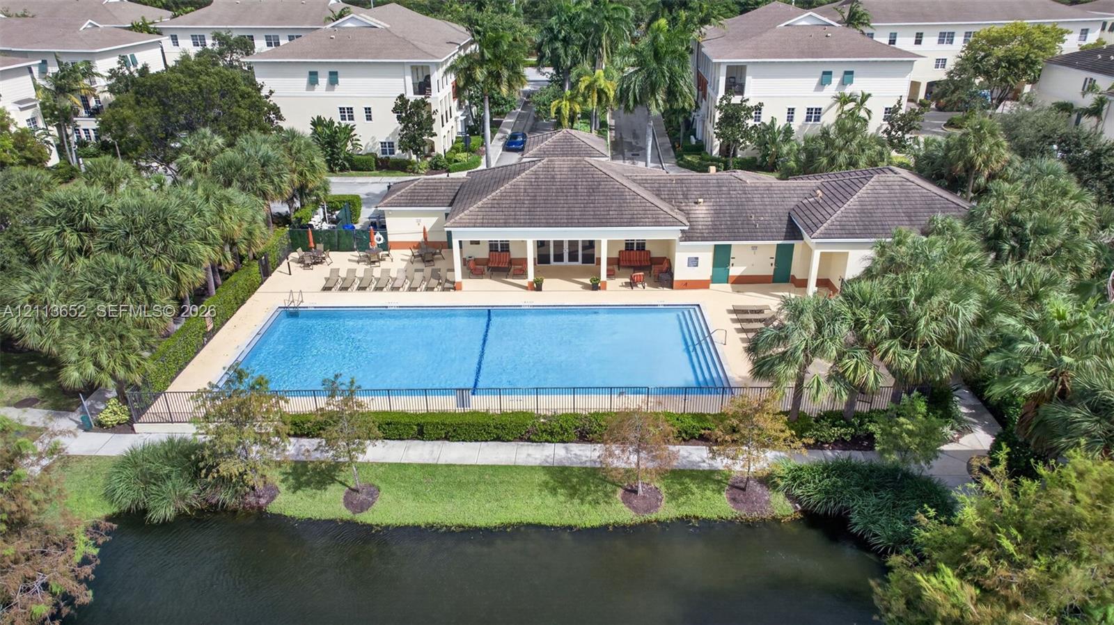 Community swimming pool featuring a concrete deck and perimeter fencing, situated near a pond with mature landscaping