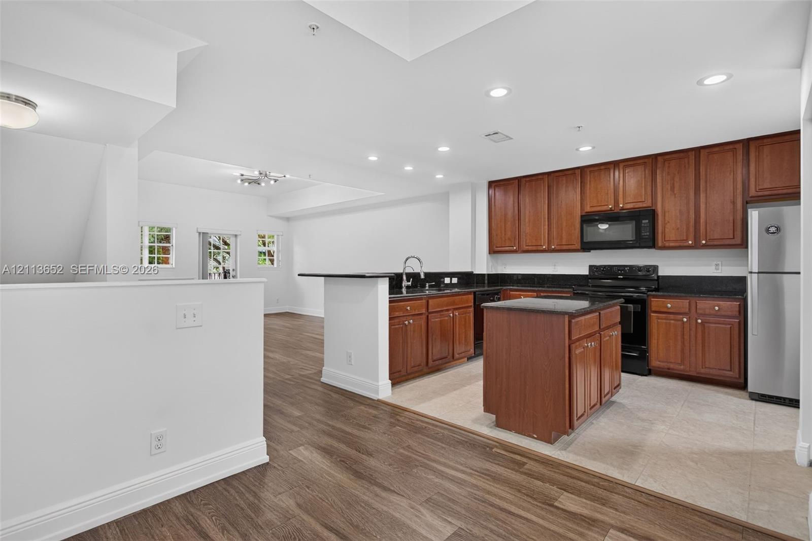 Kitchen featuring wood cabinetry, stone countertops, central island, integrated stainless steel appliances, and wood-finish flooring
