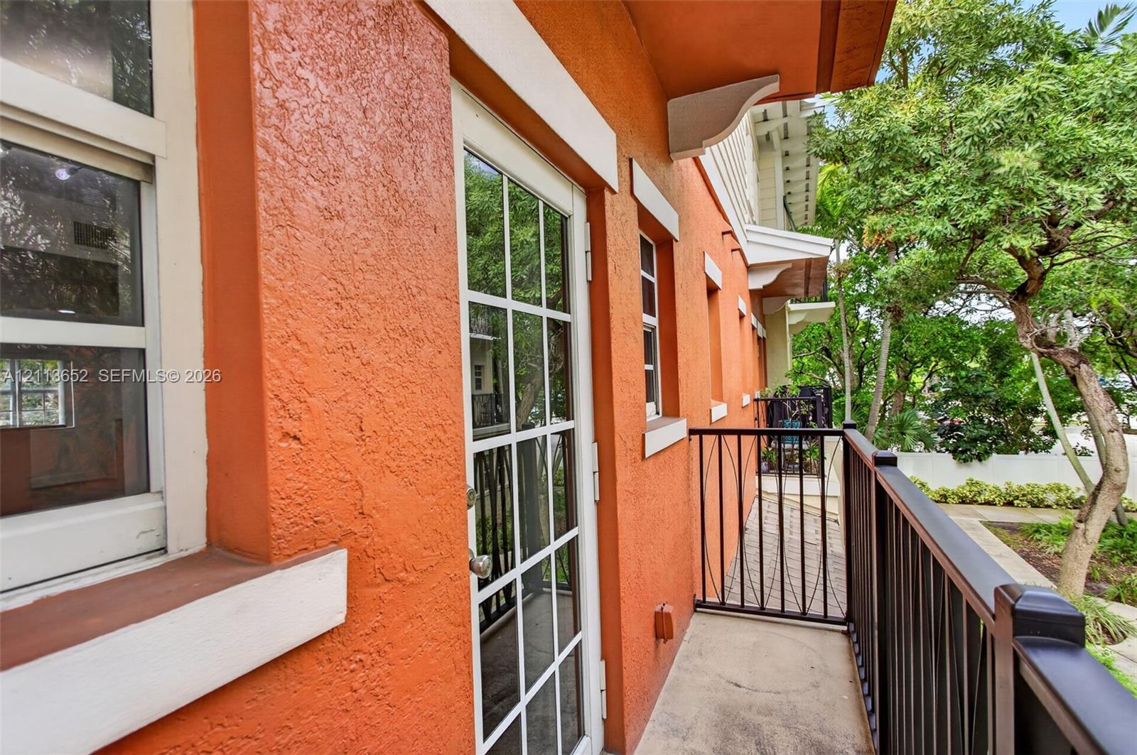 Exterior balcony featuring stucco walls, a multi-pane glass entry door, and a black metal railing