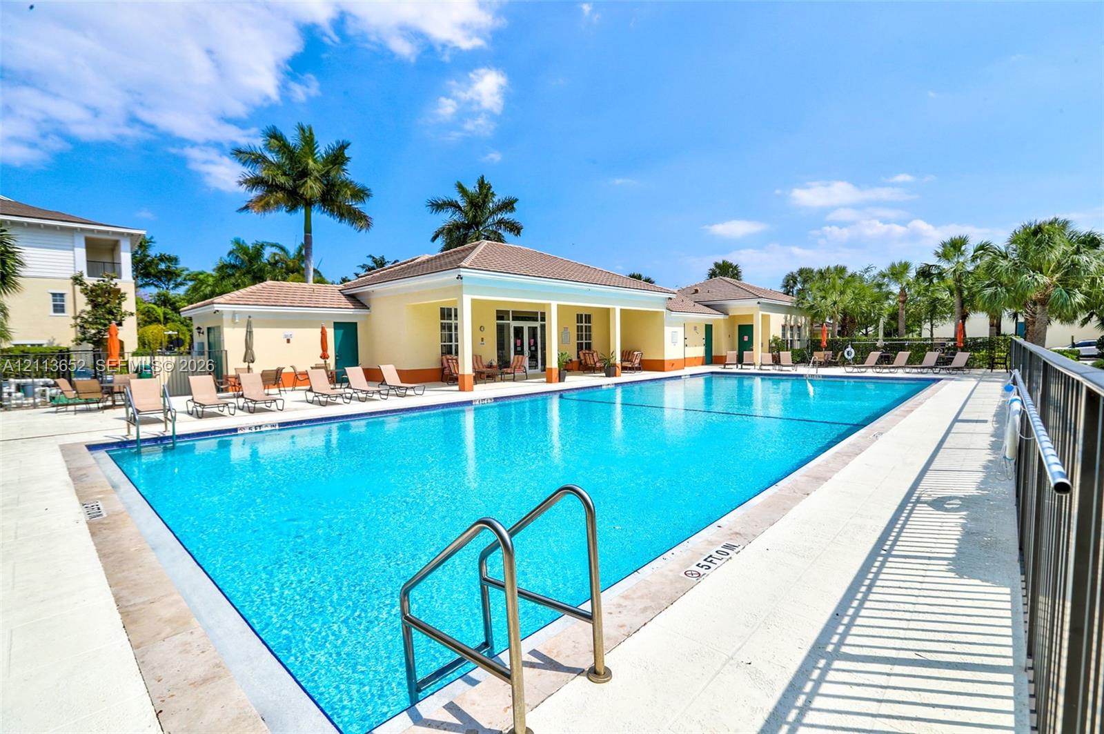 Rectangular swimming pool with metal ladder entry, surrounded by a light-toned concrete deck and an encompassing metal perimeter fence