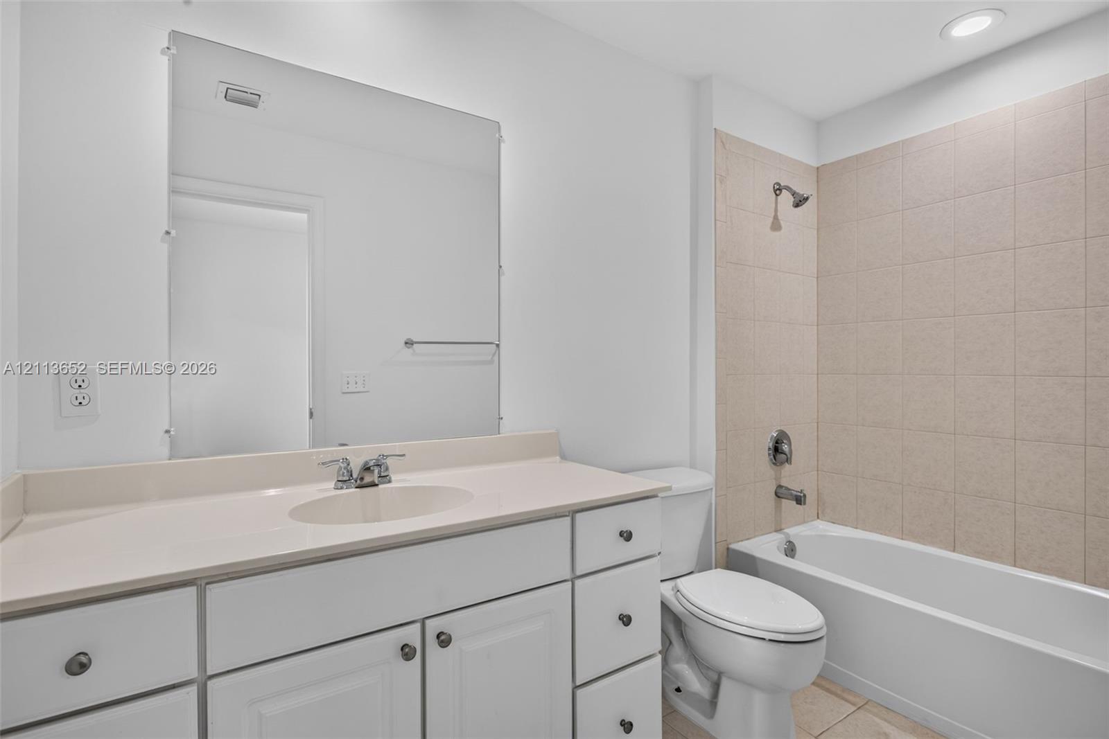 Bathroom featuring a white vanity with integrated basin, expansive wall-mounted mirror, recessed lighting, and a bathtub with tile surround