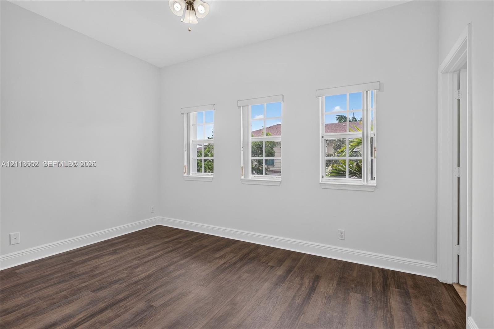Interior room featuring wood-finish flooring, three double-hung windows, and a flush-mount light fixture