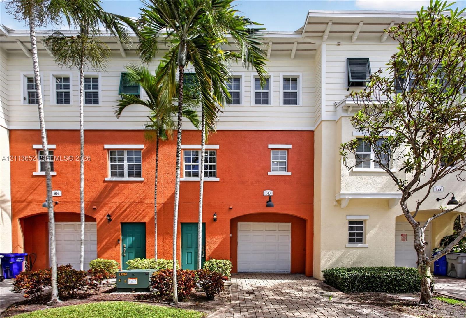 Multi-story exterior featuring a textured stucco facade, integrated single-car garages, and an overhead roofline with exposed rafters