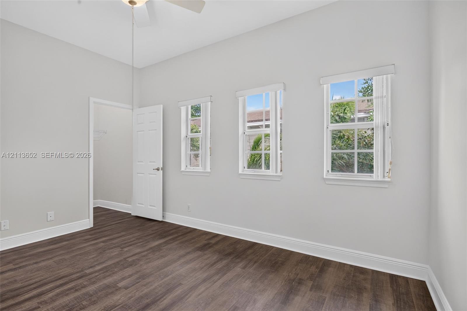 Room featuring wood-finish flooring, three grid-pane windows, and a white six-panel door