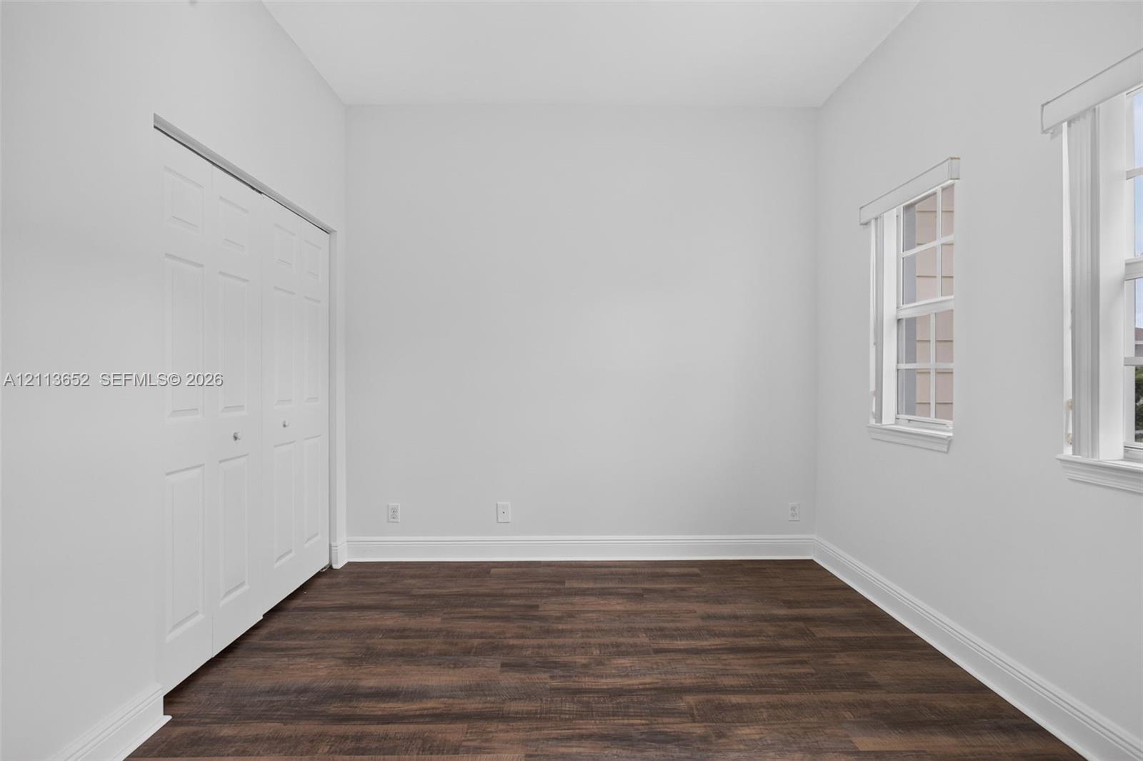 Room featuring wood-finish flooring, neutral walls, double-door closet, and dual windows