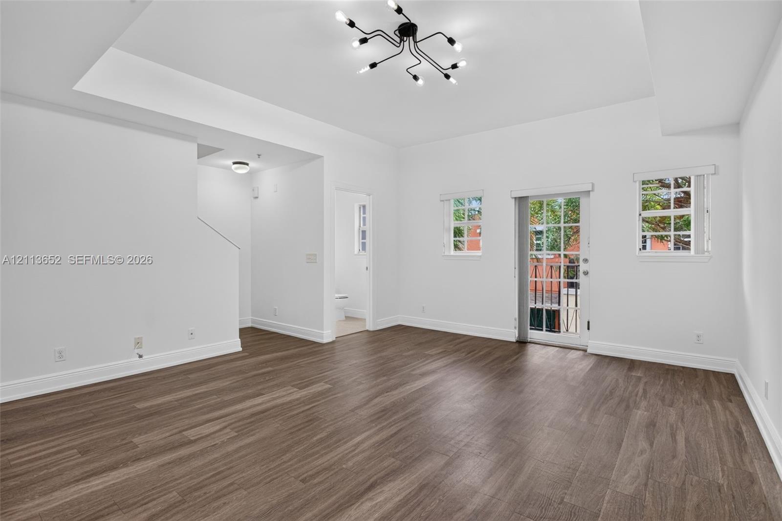 Living area featuring wood-finish flooring, a tray ceiling, a multi-arm modern chandelier, and a glass-paneled door