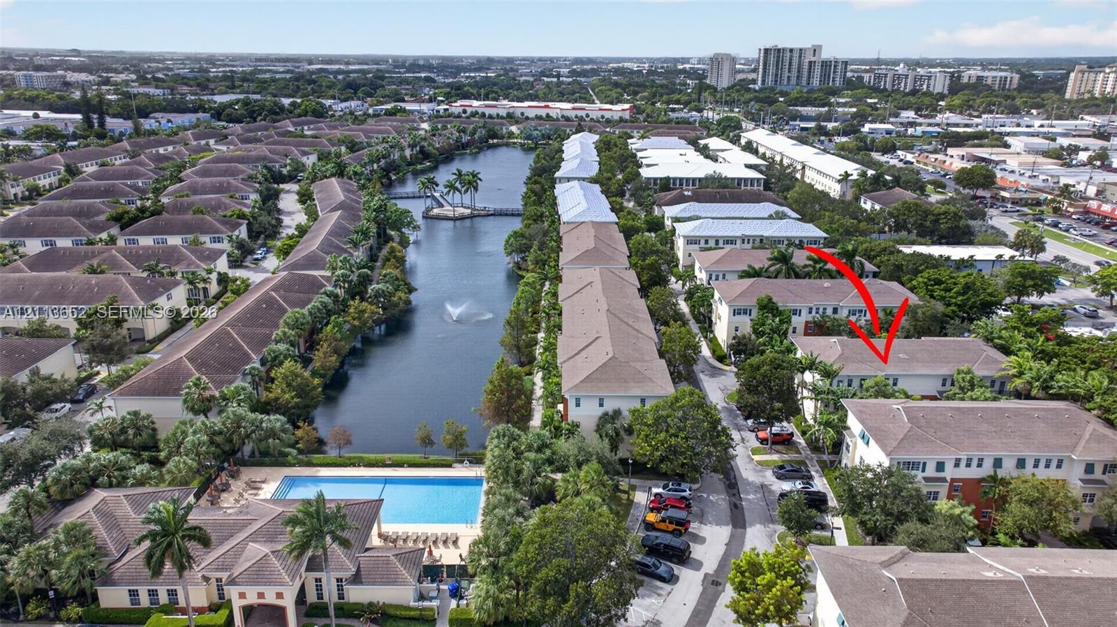 Aerial perspective of residential community featuring a multi-story building, an expansive water feature with a fountain, a swimming pool, and mature palm trees