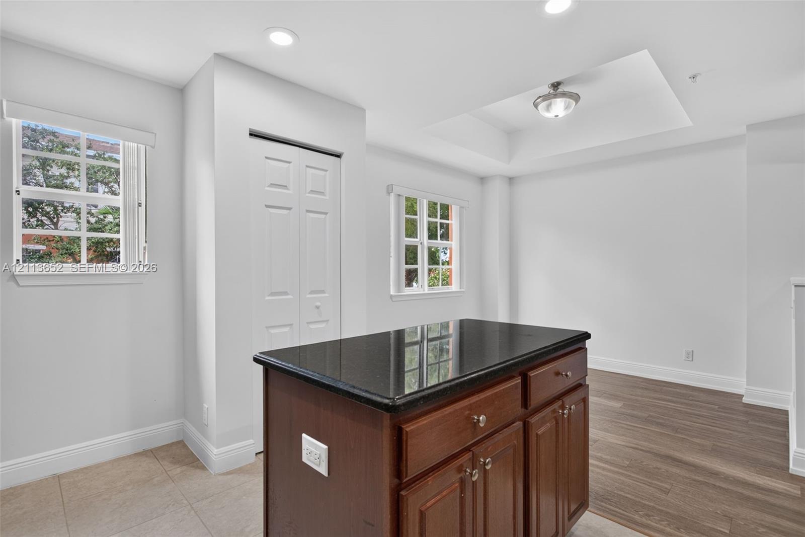 Kitchen island with a dark stone countertop and wood-finish cabinetry, recessed ceiling lighting, tray ceiling detail, dual-pane windows, and wood-finish flooring