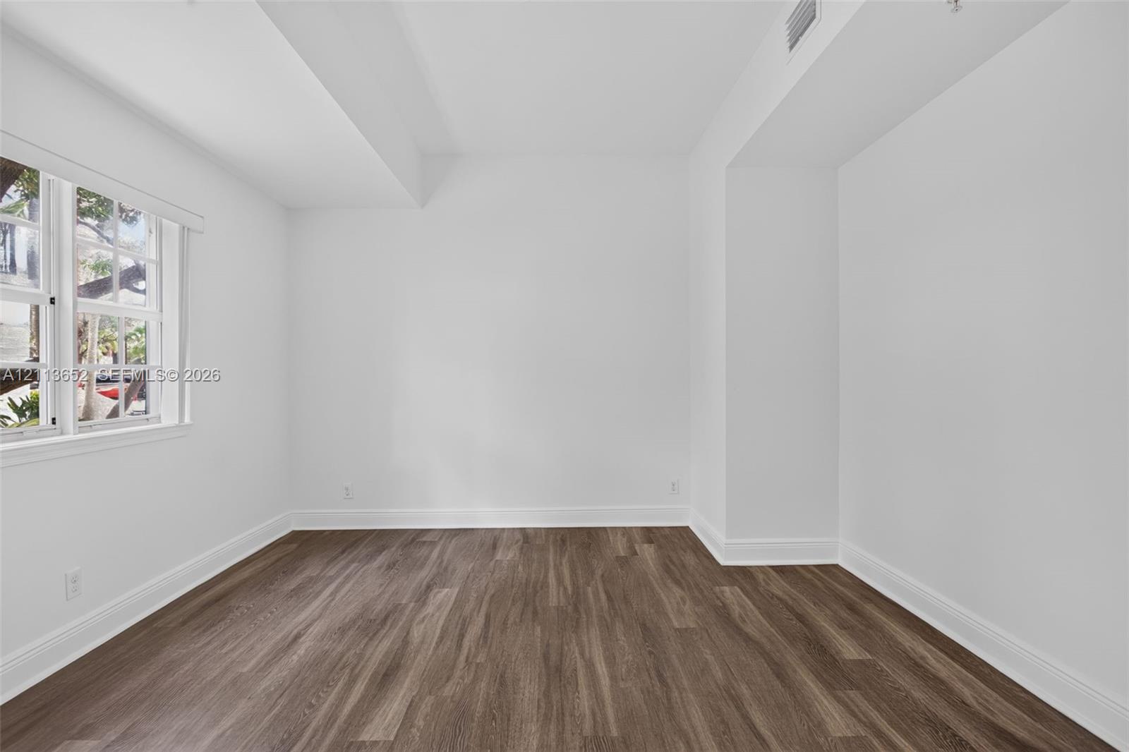 Room featuring wood-finish flooring, crisp white walls, and a multi-pane window